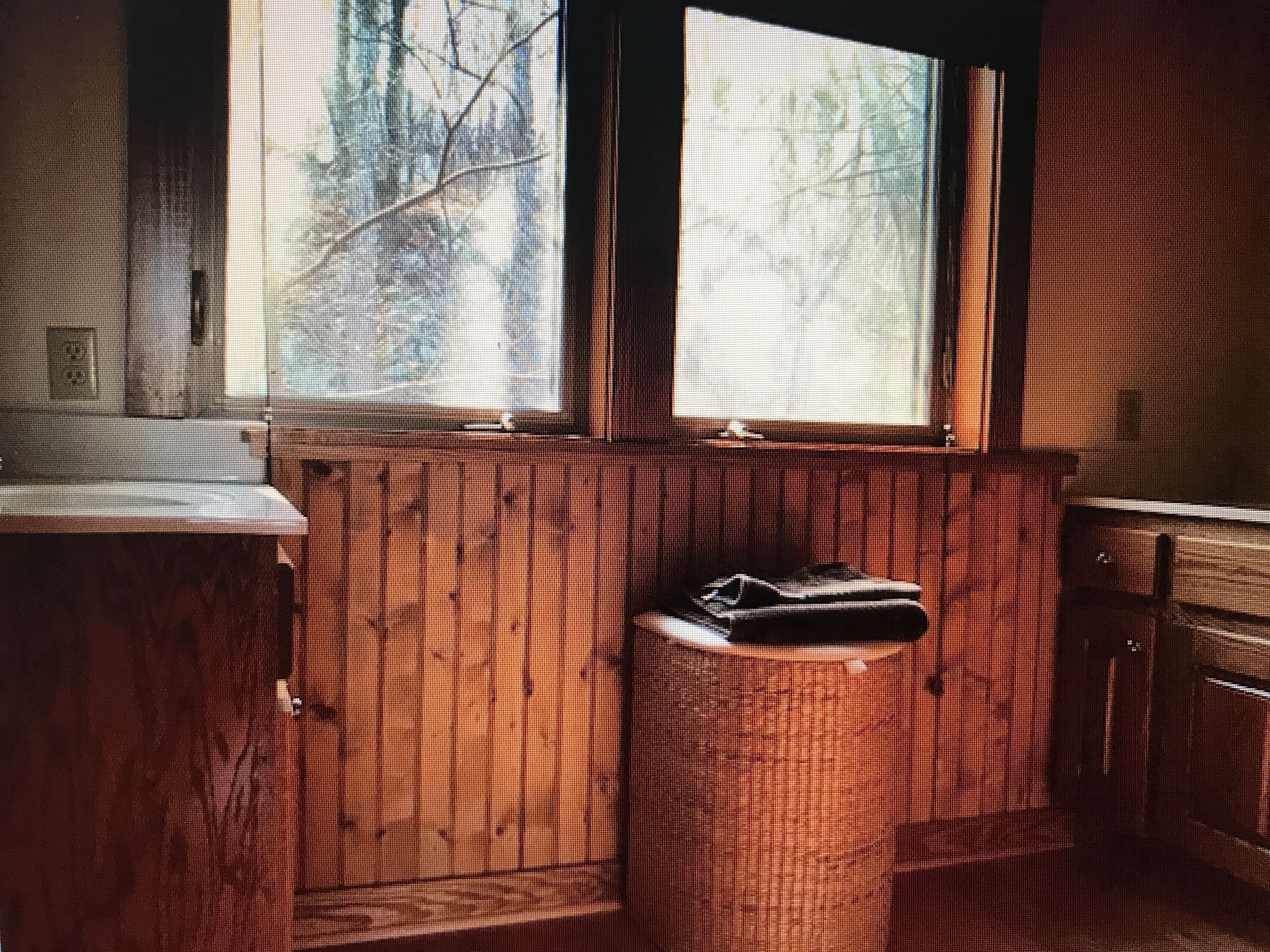 Interno di una casetta in legno con una finestra, un lavandino e un cestino.
