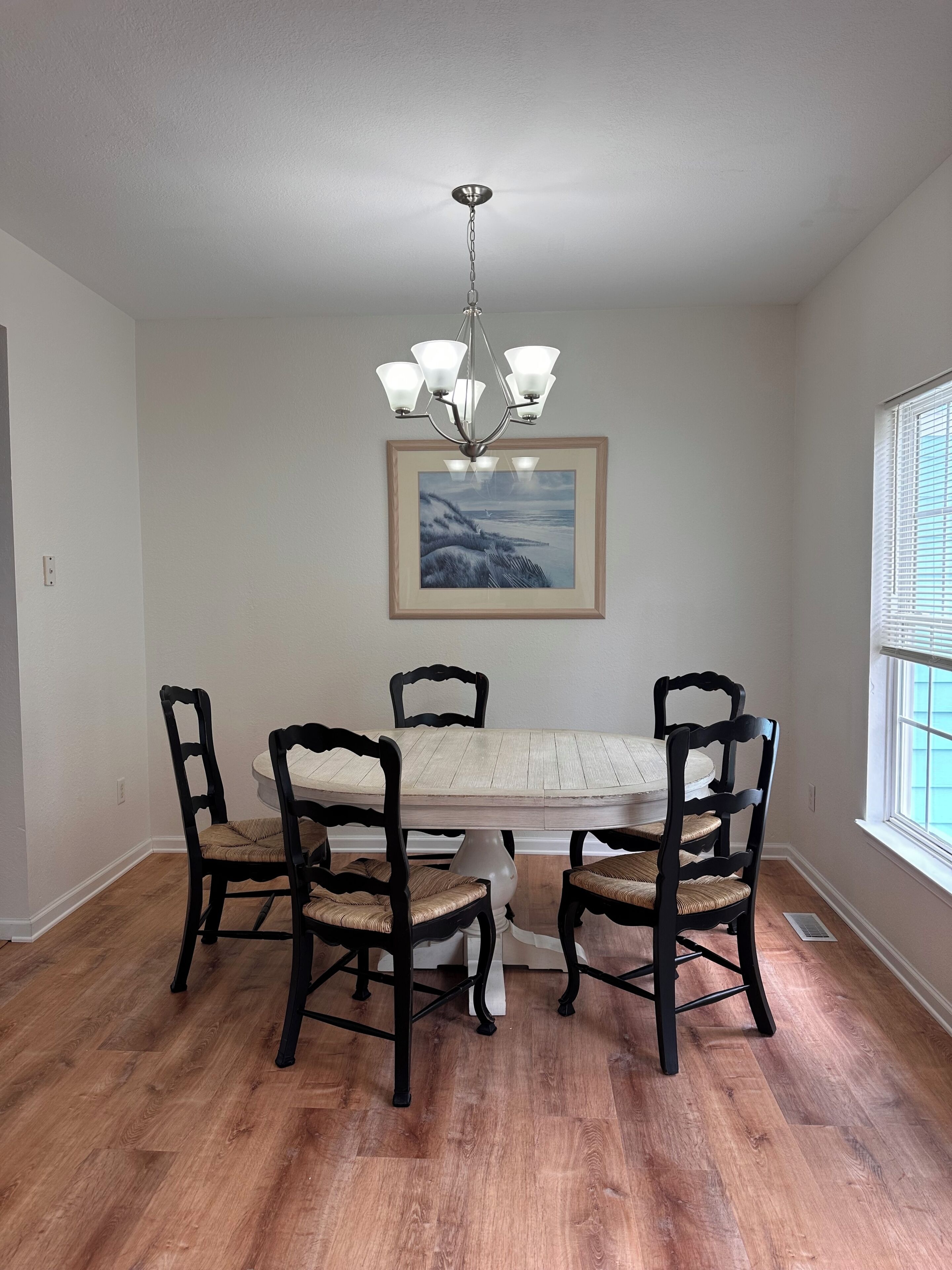 Une salle à manger avec une table en bois, quatre chaises, un lustre et un tableau encadré au mur.