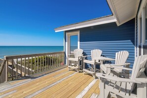 Una terraza de madera con sillas blancas y una mesa con vista a la playa.