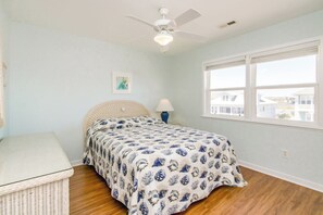 Een slaapkamer met een bed, een plafondventilator, een raam en een rieten mand.