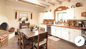 Una cocina rústica con vigas de madera, armarios blancos y piso de piedra.
