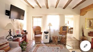 Una sala de estar acogedora con una televisión de pantalla plana, sillas de mimbre, un tapete estampado y una chimenea.