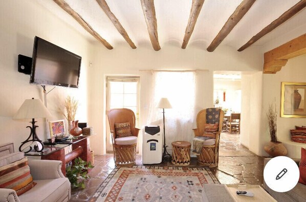 A cozy living room with a flat-screen TV, wicker chairs, a patterned rug, and a fireplace.