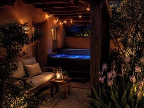 A hot tub area with a wooden bench and a table, surrounded by plants and string lights.