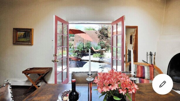 Una habitación con techo de madera, una mesa con una botella y flores, y vistas a un jardín exterior con un paraguas rojo.