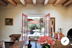 Una habitación con techo de madera, una mesa con una botella y flores, y vistas a un jardín exterior con un paraguas rojo.
