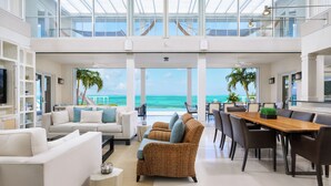 A spacious living area with a view of the ocean, featuring a white sofa, a wicker armchair, and a dining table with chairs.