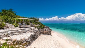 A beach with a stone staircase leading to a seating area with umbrellas.
