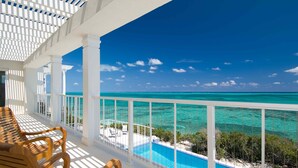 A balcony with a view of a clear blue ocean and a swimming pool.