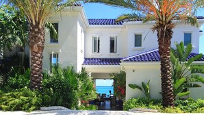 A two-story building with a white facade and blue-tiled roof, surrounded by lush greenery and palm trees.