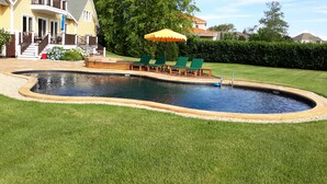 A swimming pool with a hot tub, surrounded by a deck with lounge chairs and an umbrella.