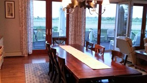 A dining room with a wooden table and chairs, a chandelier, and large windows with a view of the outdoors.