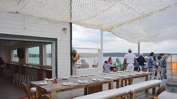 A wooden deck with tables and benches, overlooking a body of water.