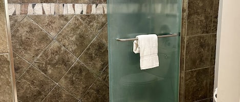A bathroom with a glass-enclosed shower, a towel rack, a patterned rug, and a toilet.