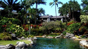A tropical resort with a clear pool, lush greenery, and a two-story building with balconies. - Stunning Views of Hanalei Bay and Bali Hai | Kauai North Shore (Princeville)