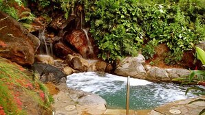 A stone pool with a waterfall, surrounded by rocks and greenery. - Stunning Views of Hanalei Bay and Bali Hai | Kauai North Shore (Princeville)