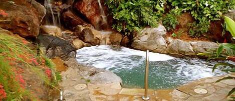 Una piscina de piedra con cascada, rodeada de rocas y vegetación.
