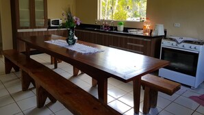 A kitchen with a wooden table, benches, a microwave, a stove, and a window with a view of greenery. - Mogi das Cruzes Farm - SP. - 90% Atlantic Forest - Cozy!!! (15 people) (Mogi das Cruzes)