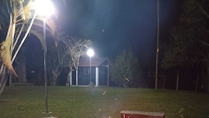 A nighttime outdoor setting with a circular fire pit in the foreground, a small building in the background, and a street lamp illuminating the area. - Mogi das Cruzes Farm - SP. - 90% Atlantic Forest - Cozy!!! (15 people) (Mogi das Cruzes)