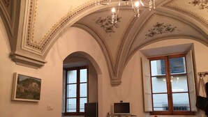 Ein Essbereich mit einem Glastisch, Stühlen, einem Gemälde an der Wand und einem Fernseher auf einem kleinen Tisch.