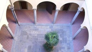 Ein Innenhof mit einer zentralen Palme, umgeben von Bögen und Steinplatten.