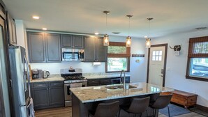 Une cuisine moderne dotée de plans de travail en granit, d’appareils électroménagers en acier inoxydable et d’un îlot central avec des tabourets de bar.