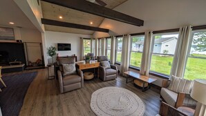 Un salon spacieux doté d’une cheminée, de sièges confortables, d’une table en bois et de grandes fenêtres offrant une vue sur l’extérieur.