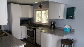 A kitchen with white cabinets, a microwave, a stove, a coffee maker, and a window with a view of trees.