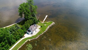 An aerial view of a house with a dock extending into a lake, surrounded by lush greenery. - The Little Lake House - Private/Secluded Pennisula - Lake Winnebago (Fond du Lac)