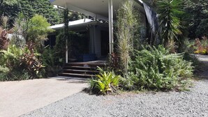 A modern house with a covered porch, surrounded by lush greenery and a gravel driveway. - Daintree Holiday Accommodation (Cow Bay)