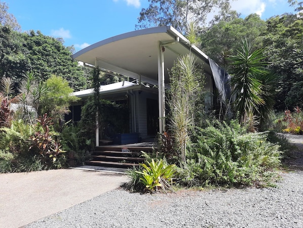 A modern house with a covered porch, surrounded by lush greenery and a gravel driveway. - Daintree Holiday Accommodation (Cow Bay)