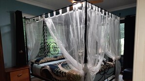 A four-poster canopy bed with a decorative headboard, a bedside table, and a nightstand. - Daintree Holiday Accommodation (Cow Bay)