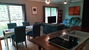 A dining area with a table and chairs, a kitchen with a sink and stove, a sofa, and a ceiling fan. - Daintree Holiday Accommodation (Cow Bay)