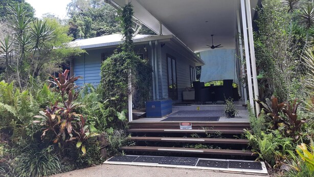 A modern house with a covered porch, steps leading to a seating area, and lush greenery surrounding the property. - Daintree Holiday Accommodation (Cow Bay)
