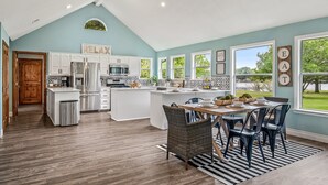 A spacious kitchen with a central island, white cabinetry, and a dining area with wicker chairs. - 4th Nt Free! Waterfront Bungalow! Dock | Kayaks (Wills Point)