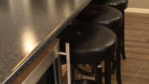 Une cuisine avec un plan de travail noir, un évier en acier inoxydable et des armoires en bois. On y trouve trois tabourets de bar noirs avec des pieds en métal.