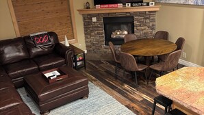 Una sala de estar con chimenea de piedra, sofá de cuero, mesa de comedor y televisor colocado sobre la chimenea.