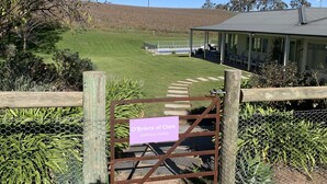 A gated entrance to O'Brien's of Clare Spring Farm with a sign, a covered outdoor seating area, and a view of the farm fields. - Vineyard views, large deck, Pet friendly, WiFi, Netflix, Pool, Firepit, Aircon (Spring Farm)
