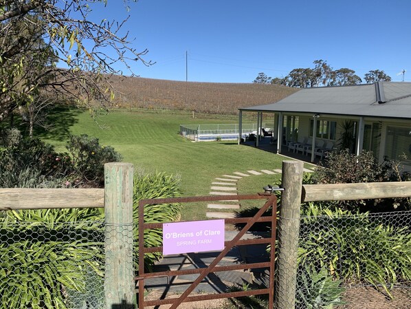A gated entrance to O'Brien's of Clare Spring Farm with a sign, a covered outdoor seating area, and a view of the farm fields. - Vineyard views, large deck, Pet friendly, WiFi, Netflix, Pool, Firepit, Aircon (Spring Farm)