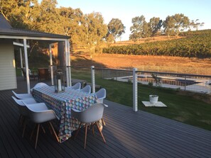 A deck with a table and chairs, overlooking a landscaped garden and a fence. - Vineyard views, large deck, Pet friendly, WiFi, Netflix, Pool, Firepit, Aircon (Spring Farm)