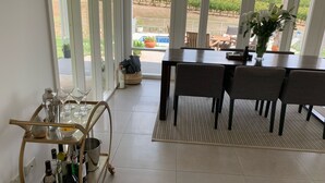 A dining area with a table and chairs, a cart with bottles and glasses, and a view of a vineyard through large windows. - Vineyard views, large deck, Pet friendly, WiFi, Netflix, Pool, Firepit, Aircon (Spring Farm)
