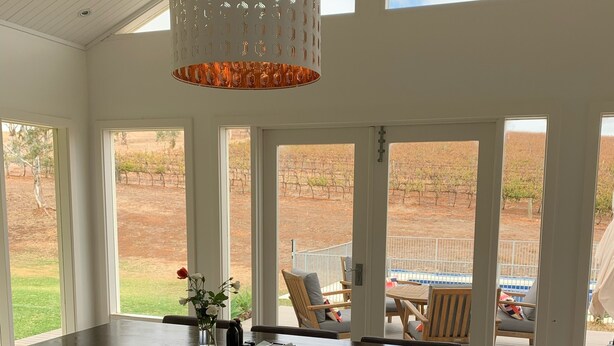 A dining area with a large table, chairs, and a hanging light fixture. - Vineyard views, large deck, Pet friendly, WiFi, Netflix, Pool, Firepit, Aircon (Spring Farm)