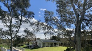 A house with a covered patio, a swimming pool, and a well-maintained lawn. - Vineyard views, large deck, Pet friendly, WiFi, Netflix, Pool, Firepit, Aircon (Spring Farm)
