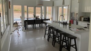 A modern kitchen with a central island, bar stools, and large windows offering views of the outdoors. - Vineyard views, large deck, Pet friendly, WiFi, Netflix, Pool, Firepit, Aircon (Spring Farm)