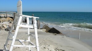 Une plage avec une chaise de maître-nageur blanche, des rochers et l’océan.