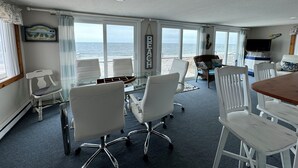 Une pièce avec vue sur l’océan, des chaises blanches, une table en bois et un téléviseur.