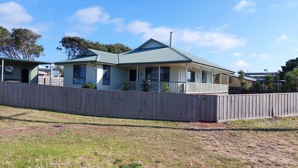 A single-story house with a porch, a fenced yard, and a clear sky.