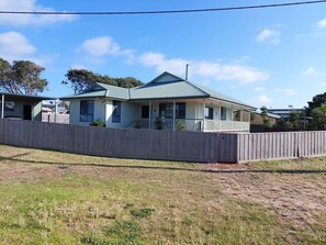 A single-story house with a porch, a fenced yard, and a clear sky.