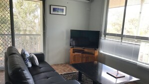 A living room with a black leather sofa, a wooden coffee table, and a flat-screen TV on a stand.