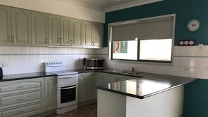 A kitchen with white cabinets, a stove, a microwave, and a window with blinds.